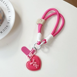 Close-up of pink braided phone lanyard with heart charm and leather smiley face accent