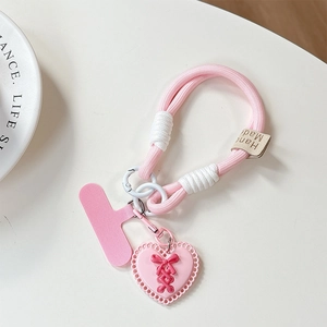 Pink braided phone lanyard with a heart pendant and bow detail on a white desk