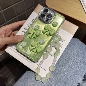 Detailed close-up of glitter iPhone case with 3D bows, floral charms and green bead strap