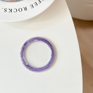 Macro shot of a purple glitter phone camera lens ring with silver edges on a white base