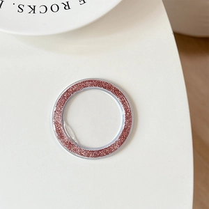 Macro shot of pink glitter phone camera lens protector ring on white desktop