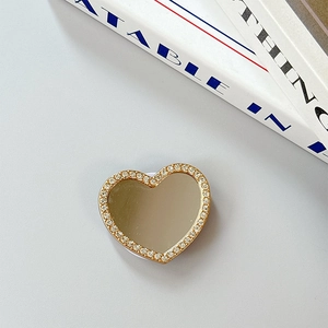 Macro view of heart-shaped phone grip featuring a compact mirror and rhinestone border