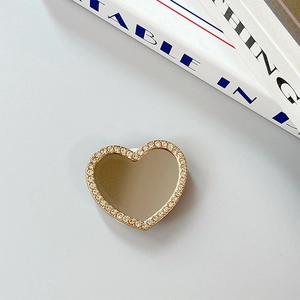 Macro shot of heart-shaped phone grip with silver mirror and rhinestones on gold base