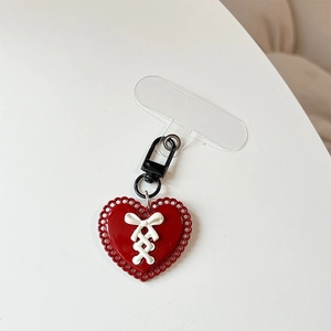 Détail du bijou de téléphone cœur rouge avec nœud blanc et fermoir noir sur gris