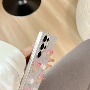Detail view of 3D resin strawberry and floral charms on a clear glitter phone case