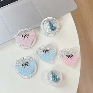 Glitter heart and 3D Christmas tree phone grip holders on desk with laptop background