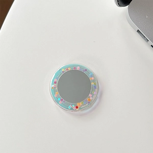 Detailed view of a circular colorful glitter mirror phone grip on a white desk surface