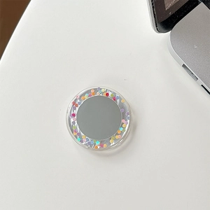 Close-up of a round silver mirror phone grip with colorful sequins on a desk