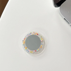 Macro view of a round acrylic mirror phone socket with colorful polka dots on a white desk