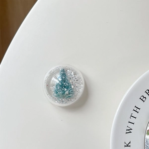 Macro shot of circular phone stand featuring a teal Christmas tree and silver glitter