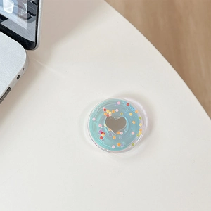 Macro shot of mint green phone grip with heart mirror and colorful sequins on white desk