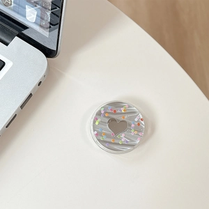 Detail of glittery heart phone grip with colorful dots on a white minimalist desktop
