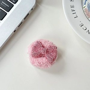 Detail of pink plush phone grip with sparkling rhinestone bow on a desktop
