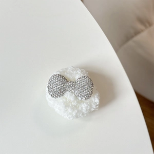 Close-up of plush bear phone socket with sparkling rhinestone bow on soft white base