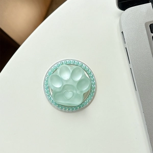 Detailed view of mint green cat paw phone grip with crystal border on a white table