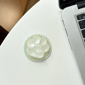 Detail view of cat paw phone grip with heart center and green pearls on silver laptop