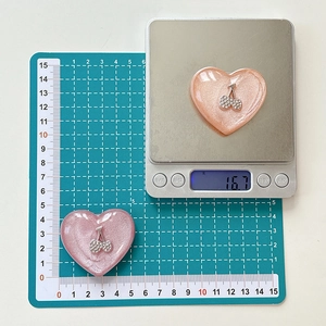 Close-up of glitter heart phone grip with rhinestone cherry design on a digital scale
