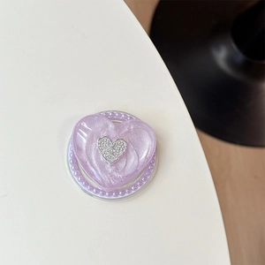 Detail einer lila glitzernden Herz-Handyhalterung mit Perlen und silbernem Metalllogo