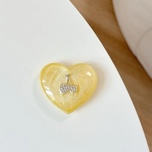 Close-up of glittery yellow heart phone grip with sparkling rhinestone cherry detail