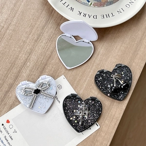 Sparkly heart-shaped portable makeup mirrors with bow and cherry decorations on wood