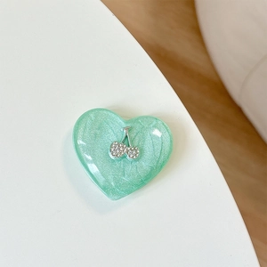 Detail of mint green resin heart phone grip featuring a sparkling rhinestone cherry design