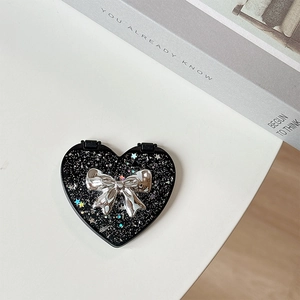 Detail of a heart-shaped portable mirror with silver glitter and a 3D metallic bow