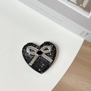 Close-up of heart-shaped portable makeup mirror with black base and silver glitter bow