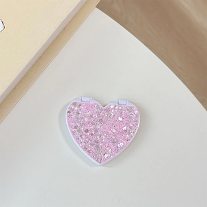Close-up of pink heart-shaped flip mirror with glitter finish on a minimal surface