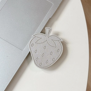 Close-up of silver leather strawberry phone stand with detailed stitching on desk