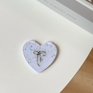 Close-up of heart-shaped purple portable makeup mirror with sequins and silver bow decoration