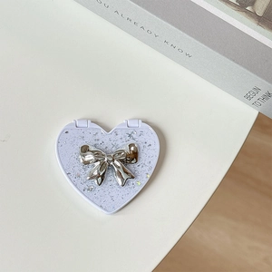 Top view of a purple heart-shaped portable mirror with silver glitter and a metal bow