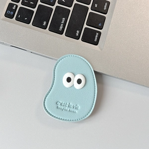 Macro view of light blue leather phone grip with cartoon eye and C'est la Vie engraving