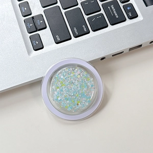 Close-up of a round clear phone socket with blue glitter sequins on a laptop surface