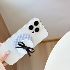 Close-up of a blue plaid phone grip with a black ribbon bow on a white smartphone