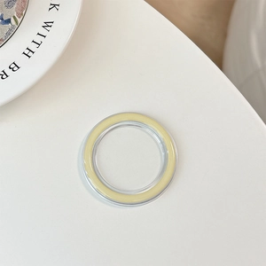 Macro detail of clear and pale yellow MagSafe magnetic ring on a minimalist white table