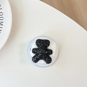 Macro detail of black rhinestone bear phone grip with soft white plush round base