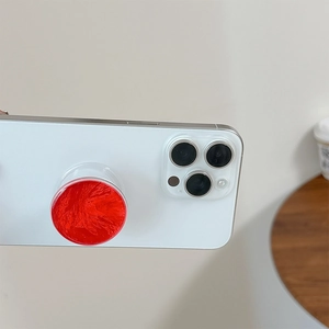 Macro detail of a red collapsible phone grip with silk texture on a white smartphone