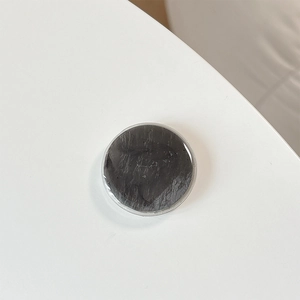 Detail of round dark gray textured phone grip with a polished glossy finish on white surface