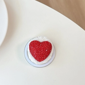 Close-up of red rhinestone heart phone grip with white plush trim on acrylic base