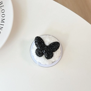 Detailed view of luxury black rhinestone butterfly on soft white plush phone grip base