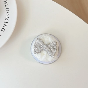 Macro view of white plush phone grip featuring a sparkling rhinestone butterfly bow detail