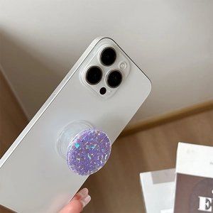Close-up of a round purple sequin phone grip holder on a white smartphone