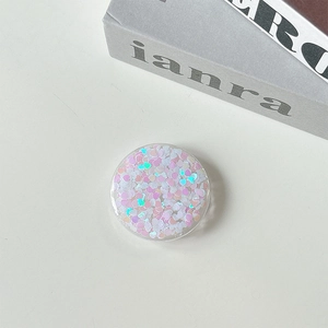 Close-up of heart-shaped glitter sequins inside a round phone grip stand on white background
