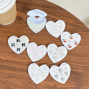 Portable heart-shaped makeup mirror set with cherry and bowknot designs on wooden table