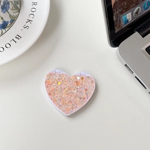 Detail of pink heart-shaped flip mirror with glitter and sequins on a desktop surface