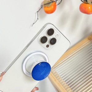 Blue round MagSafe phone socket grip on a white smartphone, minimalist scene with wood
