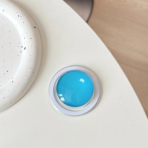 Close-up of a blue crystal glass magnetic phone grip for Magsafe on a white minimalist desk