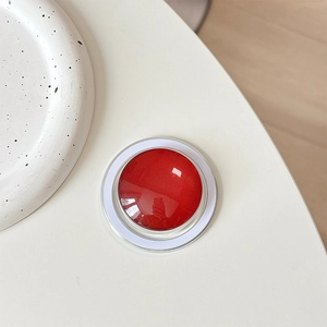 Close-up of a glossy red magnetic phone grip on a white desk with ceramic decor