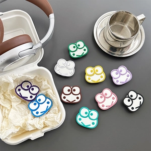 Cute cartoon frog collapsible phone grips in various colors on a modern desk setup