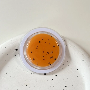 Macro shot of orange glitter gel texture with black particles on a white aesthetic tray